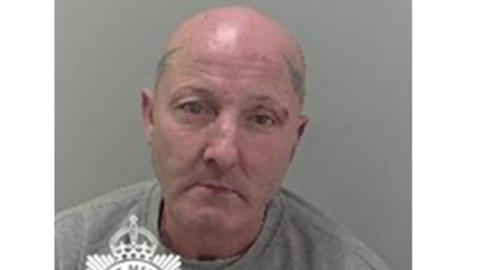 Julian Thomas in a police mugshot. He has a bald head and tattoos on both sides of his head. He is wearing a grey sweatshirt.