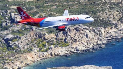 Air Malta passenger jet flying over coastline