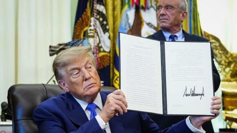 US President Donald Trump holds up an executive order he signed that aims to change childhood vaccine administration