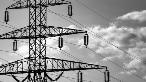 A black and white photo of pylons. There are clouds in the sky.