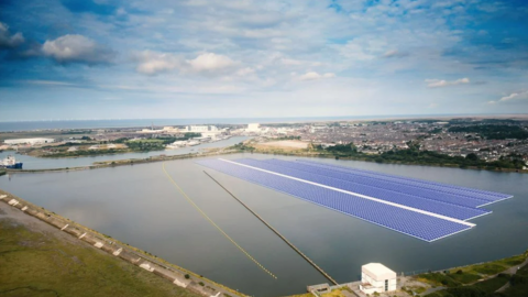 A computer generated image of four rows of solar panels floating in Barrow harbour. The town itself is behind them and there is a river connecting the dock to the sea which can just be seen behind the town