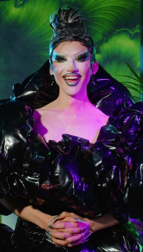 Kyran Thrax smiling at the camera whilst wearing a dress made from bin bags