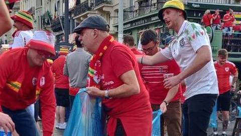 Wales fans carrying blue bags with rubbings and collecting trash on street