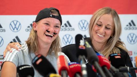 Germany's Alexandra Popp (l) wears a moustache made of kinesiotape. Kathrin Hendrich sits next to her.