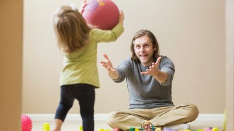 Father is holding out arms whilst a child is holding a ball.