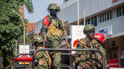 Members of Ugandan security forces stand guard outside the Uganda Parliament during an anti-corruption march in Kampala, Uganda, 23 July 2024. Four men in soldiers uniforms are seen stood on the back of a truck.