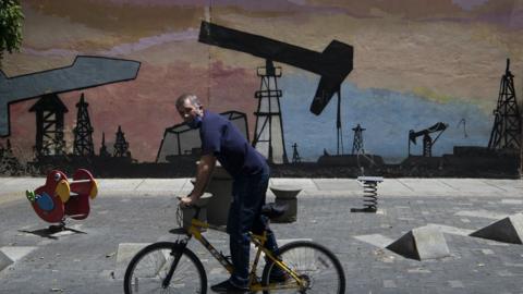 A person on a bike rides past graffiti depicting an oil drilling operation in Caracas in 2020.