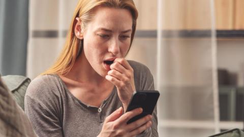 Woman looking at her phone with a shocked expression on her face.