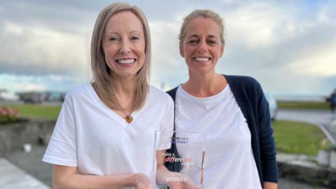 Lorna Higgins-Bare and Antonia Rainbow wearing white t-shirts and holding a glass award