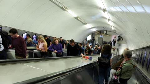 People standing on escalators as they travel up and down from the Tube platforms. 