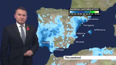 Matt Taylor stands in front of a weather map of Spain showing rainfall accumulation predictions for the weekend