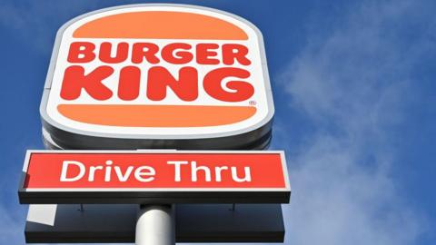 Low angle close-up of Burger King drive-thru sign against a blue sky in the background