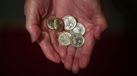 An elderly woman holding pound coins in her hands