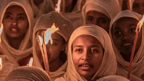 Orthodox Christian women wearing white head scarves and holding candles at prayers ahead of Christmas celebrations at the Bole Medhanialem Church in Addis Ababa - 6 January 2024