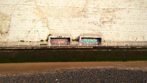 Two concrete shelters sit inside a white cliff. They are derelict and covered in graffiti. 