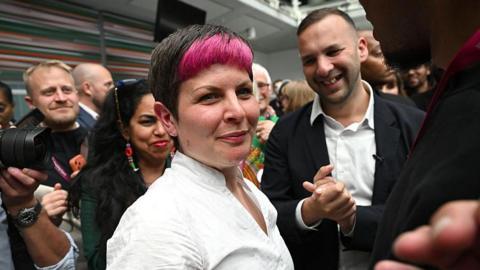 Zoe Garbett standing after victory with Zack Polanski standing behind her