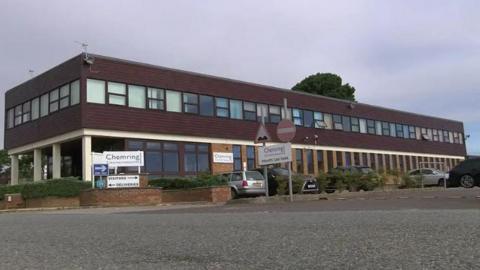 A factory with signage outside. Several cars are parked in front of the building. 