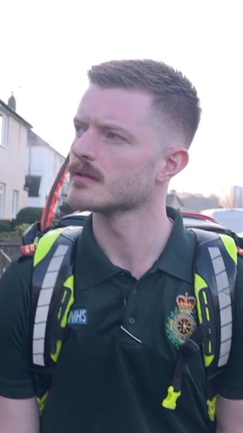 An NHS paramedic in a green t-shirt and a fluorescent rucksack walking down a street