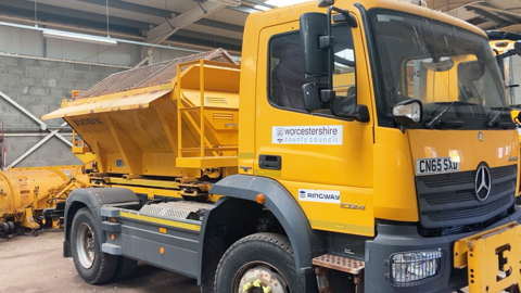 A yellow gritting lorry at a depot