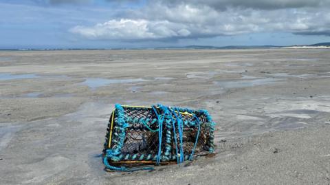 A lobster pot on the beach with grey skies behind.