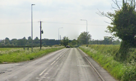 A main road, with a junction to the left, and fields and trees on either side