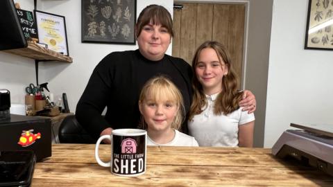 A woman stands behind a till with her daughters