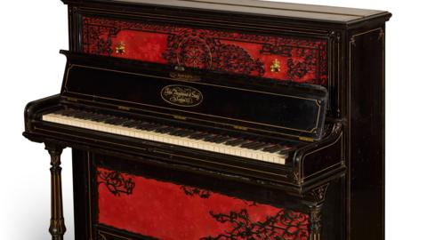 An upright piano in dark wood, with a red and black design on the front. 