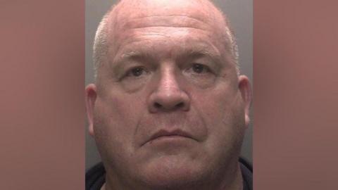 A mugshot of Mark Bocker, who is staring impassively towards the camera. 