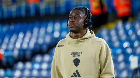 James Debayo head and shoulders shot walking across empty pitch at Elland Road wearing headphone and training top.