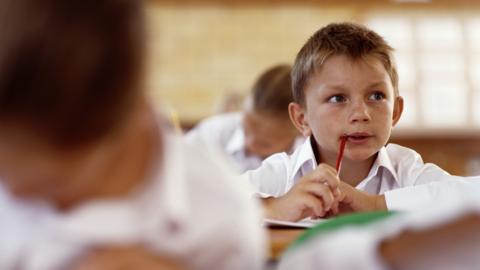 Boy in a classroom, holding pen to mouth