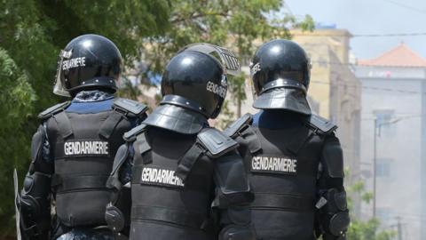 Senegalese gendarmes, in dark uniform and helmets, stand on a street corner in Dakar