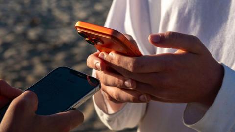 A close-up of two young men holding smartphones close together, exchanging details.