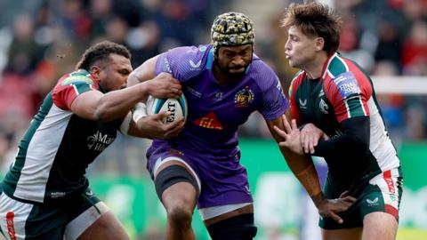 Exeter Chiefs' Christ Tshiunza bursts through the challenges of two Leicester Tigers players