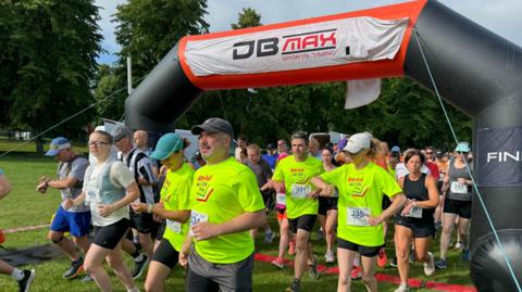 Various runners setting off from an inflatable start line, some wearing bright green tops