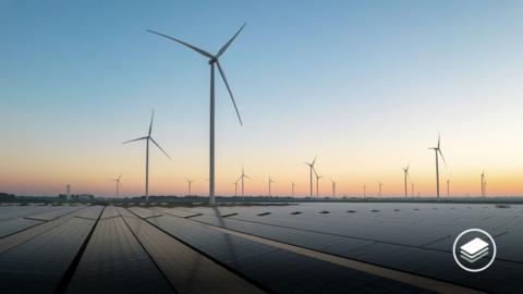 A photograph of solar energy field and wind turbines during a sunrise.