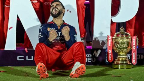 Virat Kohli cheers to himself, sat beside the IPL trophy