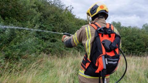 A firefighter with a backpack spraying a jet of water into a field