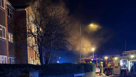 Smoke in the air, coming from a block of flats, with fire engines on the scene