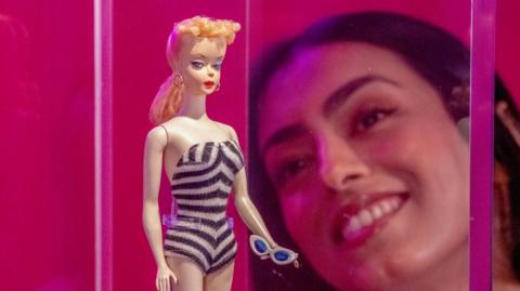 a woman looking at a vintage Barbie doll