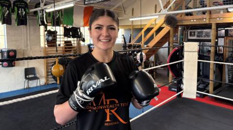 Megan Redstall raises her boxing gloves for the camera as she stands in the ring.