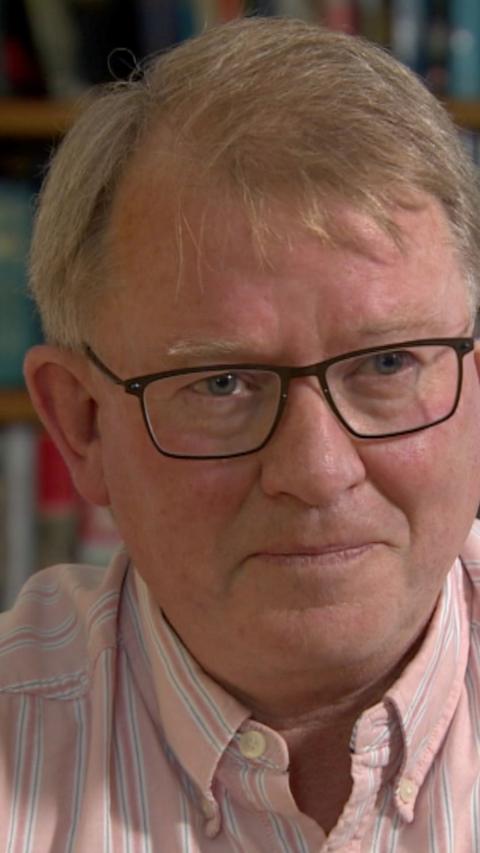 Dr Kieran McManus in pink shirt with black glasses, he has short grey hair