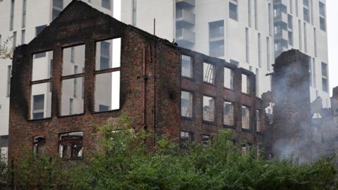 The former Hotspur Press building after a fire in Manchester, Britain, 24 June 2025. Smoke can be seen drifting up from the trees that shelter the lower levels of the multi-storey building, which was hollowed out in the blaze. 