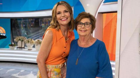 Savannah Guthrie and her mother Nancy smiling with their arms around each other in a TV news studio