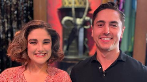 Actors Natasha Hoeberigs and Connor Carson smile at the camera while wearing their costumes for the Rocky Horror Show stage show. Natasha has short dark hair which is pinned up and Connor has dark brown styled.