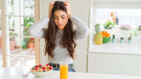 Woman holding head and looking at a bowl of food