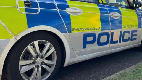 A white Norfolk Police stationary car, parked. It has writing on it, in blue and yellow boxes. 
