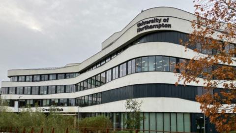 The outside of a University of Northampton building. The building is white concrete with lots of rectangular windows and says creative hub on the side of the building.