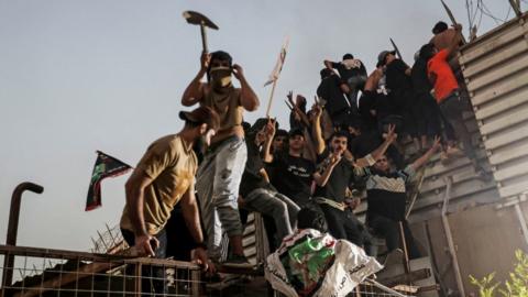 Protesters climb a fence as they gather near the Swedish embassy in Baghdad hours after the embassy was stormed and set on fire ahead of an expected Koran burning in Stockholm, in Baghdad, Iraq, July 20, 2023