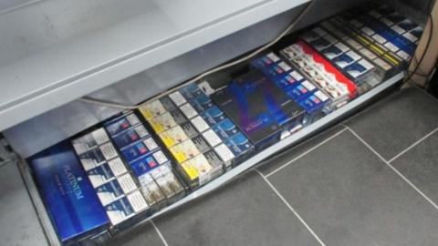 Multi-coloured packets of cigarettes in a grey metal shop tray