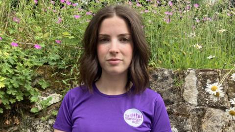 A woman with dark, short hair wearing a purple running T-shirt with a logo that reads 'The Survivors Trust'